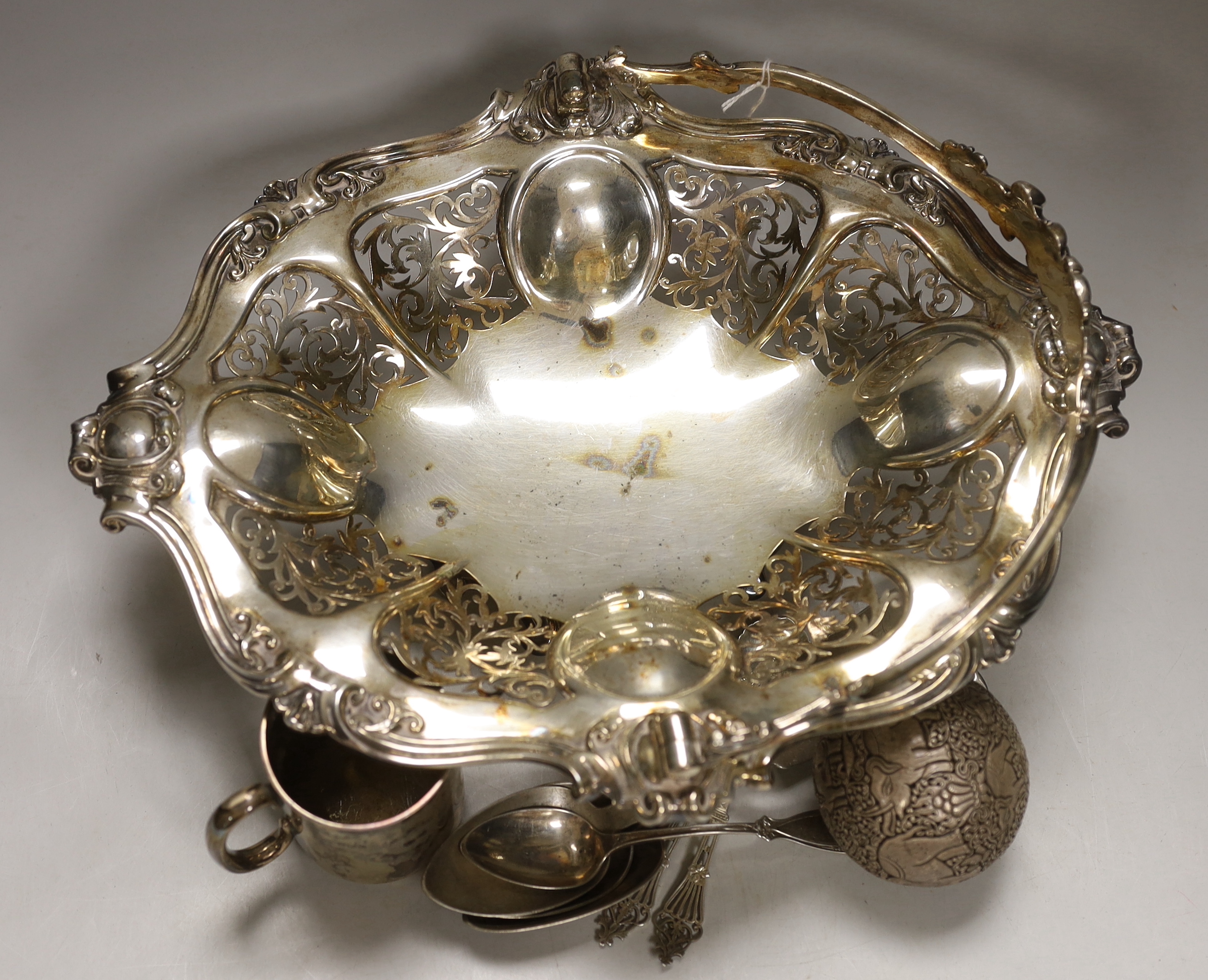 A George V silver christening mug, two silver spoons, four white metal spoons, a pierced white metal sphere? decorated with elephants and a plated bread basket.